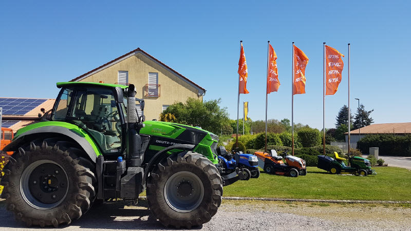 Grüner Deutz-Fahr-Traktor auf dem Hof von Franz Marz, im Hintergrund Fahnen und Rasentraktoren