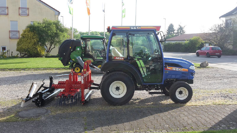 Blauer ISEKI-Kompakttraktor mit Kabine und Anbaugerät vor dem Betriebsgebäude